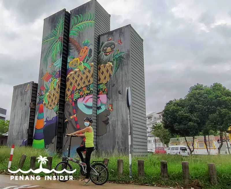 Kit cycling in front of Kanji Chai's mural realized in Karpal Singh Drive for Penang Container Art Festival 