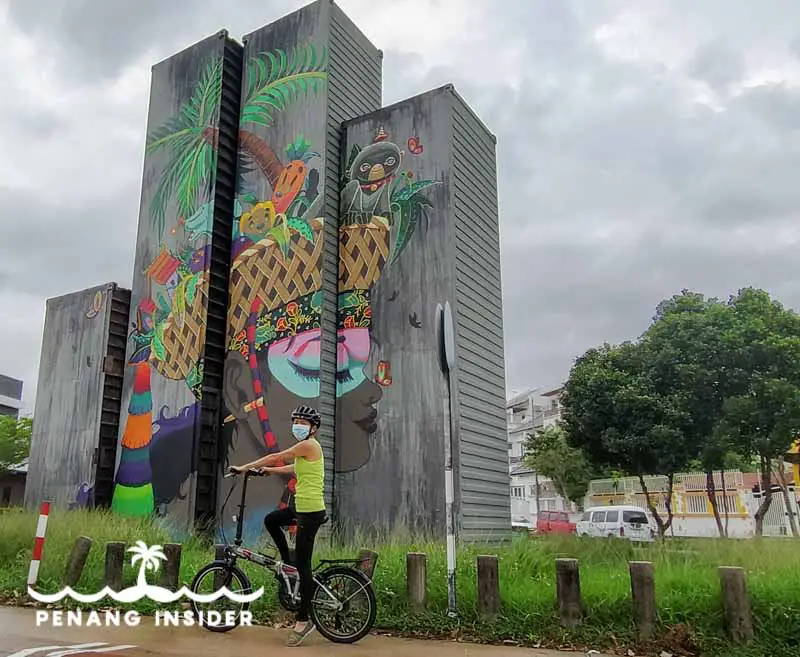 Kit cycling in front of Kanji Chai's mural realized in Karpal Singh Drive for Penang Container Art Festival